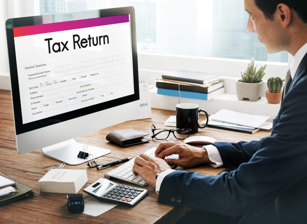 Man reviewing digital tax return form on computer with calculator and documents