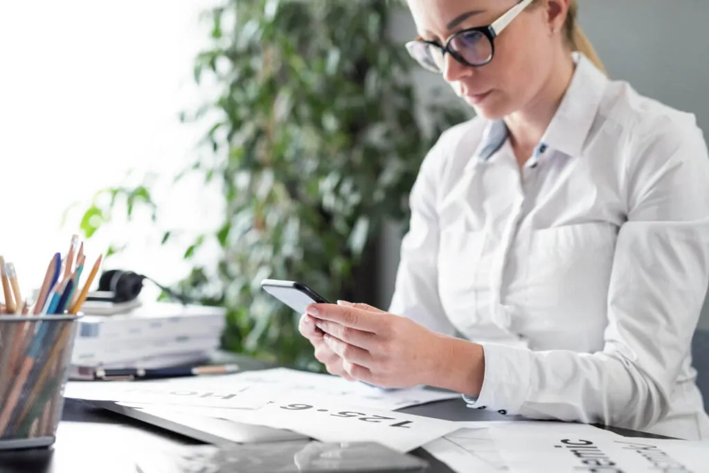 Female consultant analysing VAT registration paperwork and using a smartphone in an office setting.