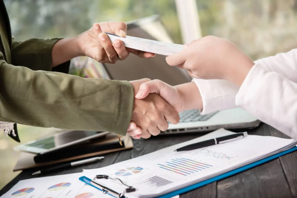 Professionals shaking hands over PAYE registration paperwork and financial charts.