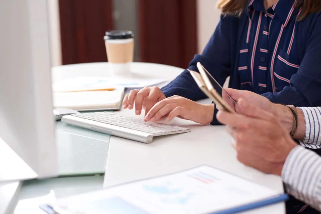 Business professionals reviewing VAT registration documents and using a mobile phone at a desk.