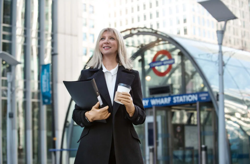 Confident businesswoman holding PAYE registration documents outside Canary Wharf Station in London.